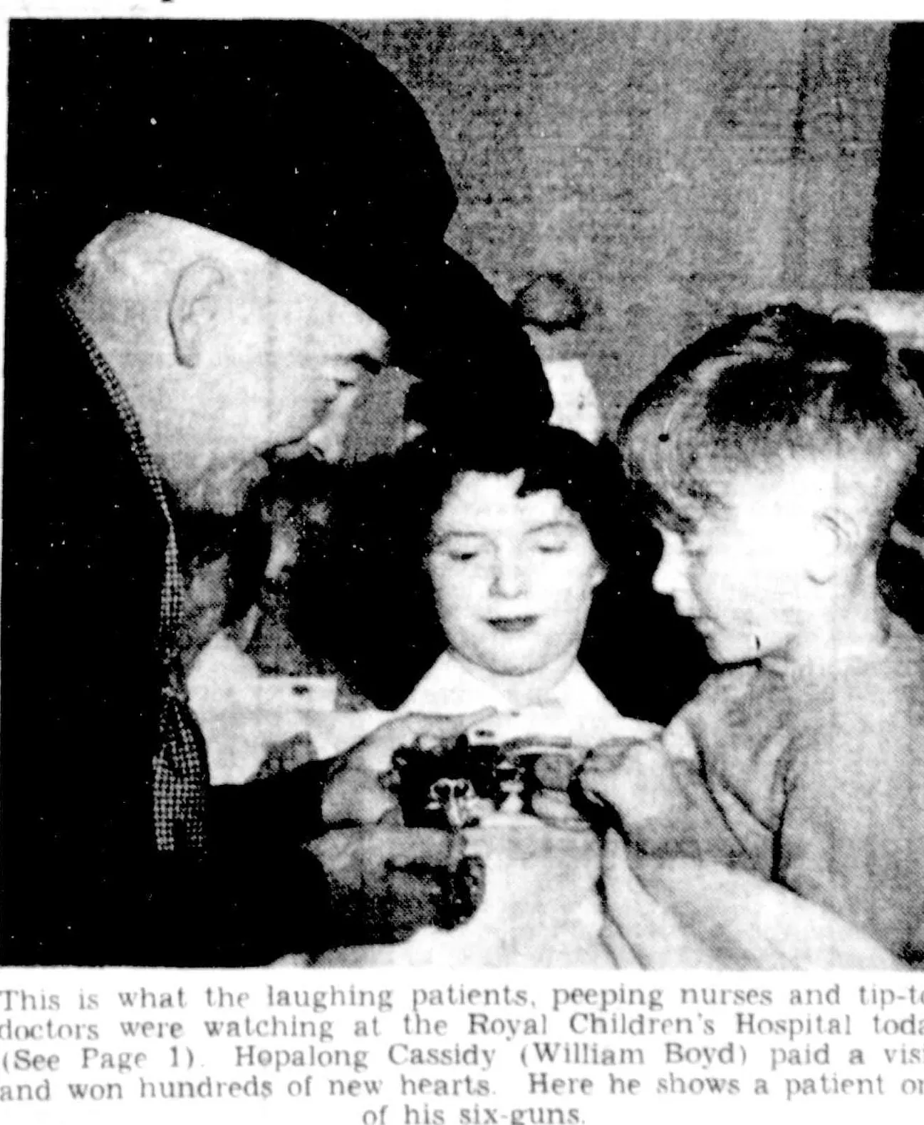 A newspaper photograph: Boyd in his black hat bends over a bed to show a six-gun to a girl and a boy. The printed caption: “This is what the laughing patients, peeping nurses and tip-toe doctors were watching at the Royal Children’s Hospital today. Hopalong Cassidy (William Boyd) paid a visit, and won hundreds of new hearts. Here he shows a patient one of his six-guns.”